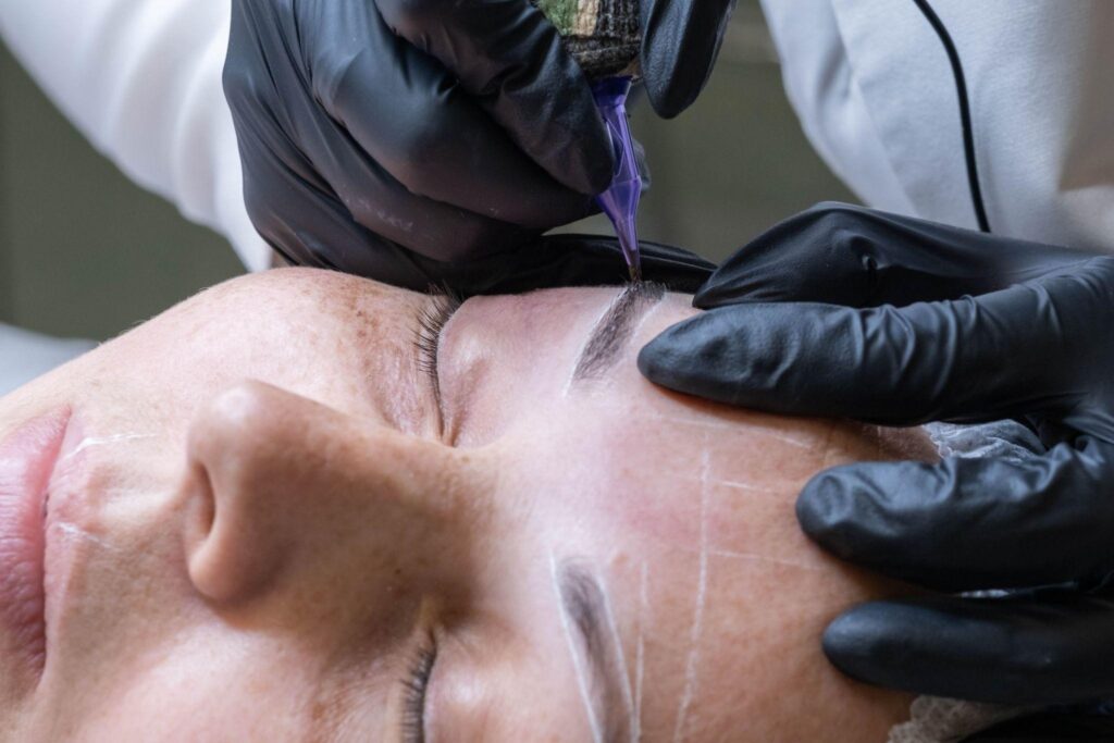 Technician performing eyebrow microblading treatment for feathered brows using precision tools and wearing black gloves
